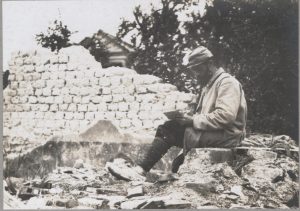Soldat écrivant au milieu des ruines de Massiges, 1914. Domaine public.